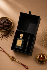 A luxury gift set featuring Mocha Muse perfume bottle with a gold cap and a black spray atomizer inside an open black presentation box, styled on a warm brown background with chocolate, a brass diya, and a red thread ornament.