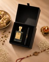 A luxury gift set featuring a clear glass perfume bottle named Nutty Affair with a gold cap and a black pen, presented inside an open black box on a beige fabric background with decorative elements like a plate of pistachio sweets, a brass candle, and a Rakhi.